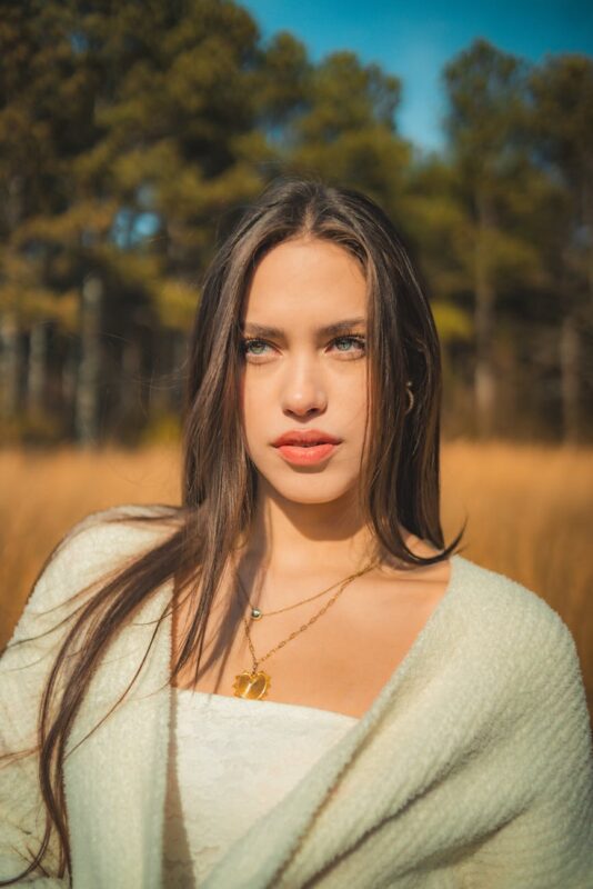 photo of a young brunette standing on a meadow in sunlight